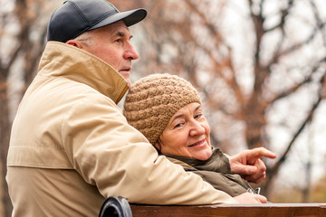 Elderly married couple sitting on a park bench on an autumn day.