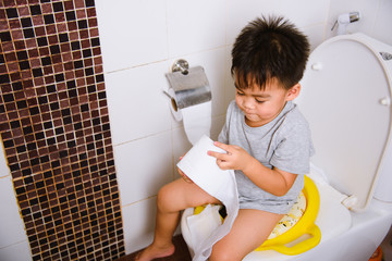 Asian little  kid 2-3 years old sitting on a kid bathroom accessory toilet