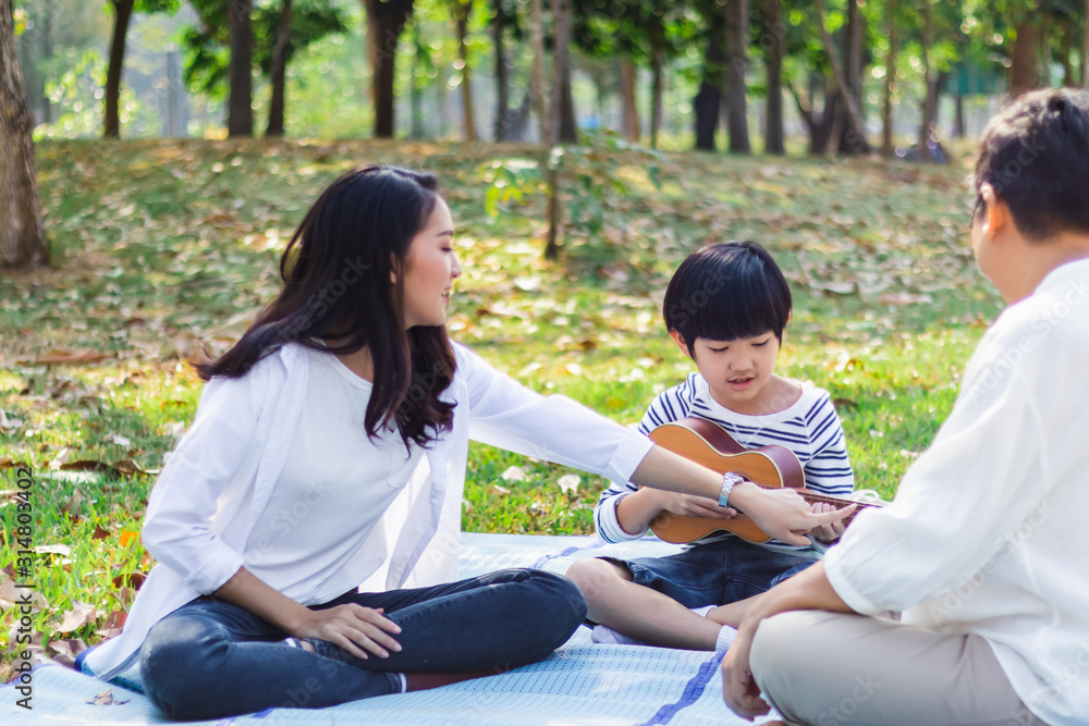 Poster Happy Asian family has leisure in the park on the weekend or holiday. Mother teach son to play guitar. Grandmother enjoy beautiful moment of love. Family generation relationship or bonding photo..