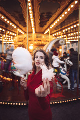 Obraz na płótnie Canvas Portrait of a beautiful young girl with white cotton candy in front of a carousel horse
