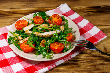 Tasty salad of fried chicken breast, fresh arugula and cherry tomatoes on wooden table
