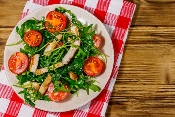 Tasty salad of fried chicken breast, fresh arugula and cherry tomatoes on wooden table. Top view