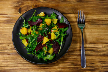 Tasty salad of fresh arugula, beetroot and oranges on wooden table. Top view. Healthy food or vegetarian concept
