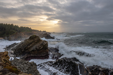 Fototapeta premium Sunset with stormy clouds and crashing waves at Shore Acres State Park, Charleston Oregon, USA