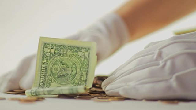 White-gloved hands scooping up a pile of gold coins. They sort out and scatter money.On white background. Garland. Money glitters.