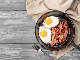 Fried eggs with bacon in a pan. Top view. Copy space.