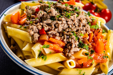 Penne with meat, tomato sauce and vegetables on wooden background