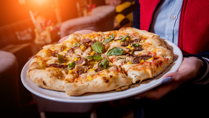 Waiter, carrying dish with tasty pizza with chicken and vegetables. Restaurant.