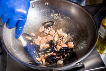Chef cooking pasta with mussels in pan. Italian style cuisine. Restaurant.