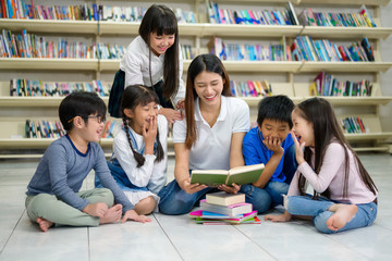 A Group of Asian Student Kid Reading a book with women teacher in School library with Shelf of Books in Background, Asian Kid Education Concept - 314809217