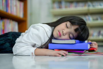 Portait of Asian Girl Sleeping on Stack of Colorful Book in School Library with Shelf of Books in Background, Asian Kid Education Concept