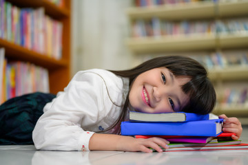 Portait of Asian Girl Sleeping on Stack of Colorful Book in School Library with Shelf of Books in Background, Asian Kid Education Concept