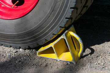 Heavy-duty yellow metal chock under the wheel of trailer with handle for easy removal. Wheel chock helps keep the truck in place on the hill