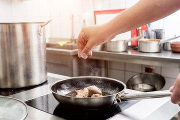 Chef cooks fried potatoes with pieces of meat in a restaurant kitchen