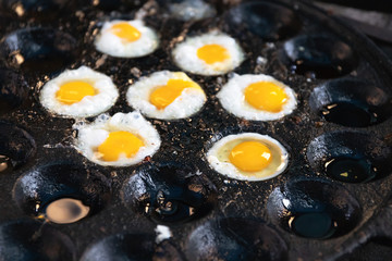 Fried Quail eggs on pothole pan. Drop each egg in a small ramekin or cup and gently slide it into the hot oil. Serve warm with salt and ground white pepper. Thai appetizer at street food market. 