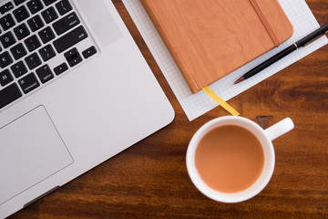 Diagonal Layflat of workspace. Self starter, meeting minutes, note taking and working as a student or at a cafe/ coffee shop on wooden table with cup of coffee/tea