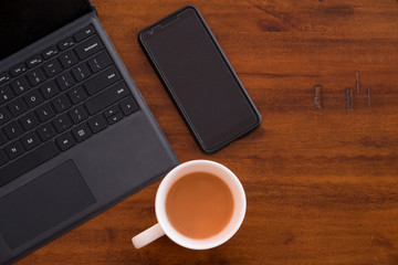Laptop keyboard with smartphone and a cup of coffee/tea on a rustic wooden table. Modern Office...
