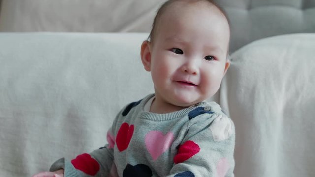 Slow motion of lovely asian baby girl sitting indoor at home looking at camera smile 9 months happy baby playing with warm sunshine on the face Chinese baby girl portrait