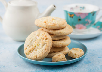 White chocolate biscuit cookies on blue ceramic plate with tea pot and cup on blue kitchen table background.