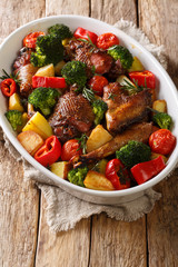 Baked homemade chicken with seasonal vegetables and herbs close-up in a baking dish on the table. vertical