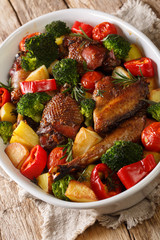 Baked pieces of chicken with potatoes, broccoli, tomatoes and pepper close-up in a baking dish on the table. vertical