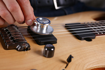 Male arms hold stethoscope head fine diagnosing classic shape wooden guitar closeup. Six stringed school education art leisure precise diagnosis electrical vintage stage shop having fun concept