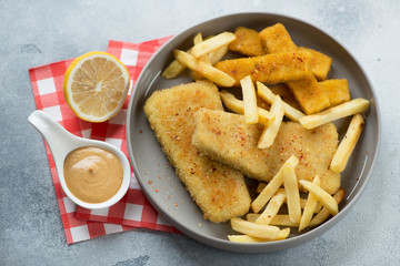 Grey plate with fish and chips or fried breaded fish fillet with french fries, elevated view, studio shot