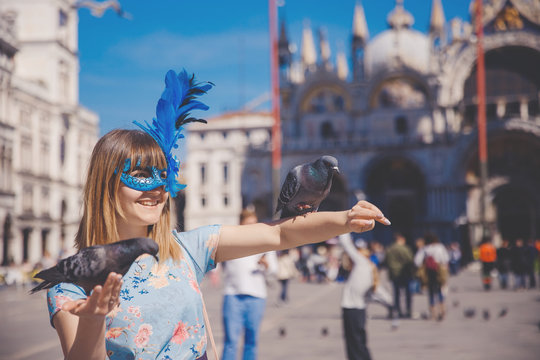 Portrait smiling young woman in Venice, Italy in Venetian mask holding pigeons on St Mark Square. Concept travel