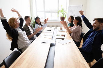 Happy corporate staff celebrating shared success seated at boardroom desk