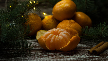 Fototapeta na wymiar Mandarins and cinnamon are on the table on new year's eve and Christmas, garland lights glow in the background