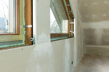 Handyman, construction man installing PVC window in a new insulated and filled dry wall attic.	