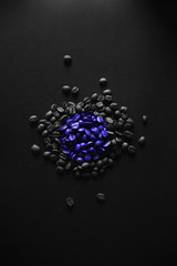 Monochrome handful of selected roasted coffee beans for morning breakfast on a black background with natural light and blue circle, creative art.