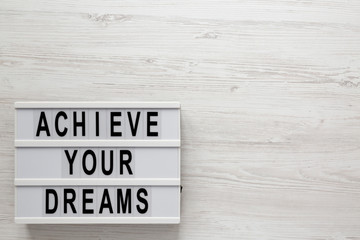 'Achieve your dreams' words on a lightbox on a white wooden surface, top view. Overhead, from above, flat lay. Copy space.