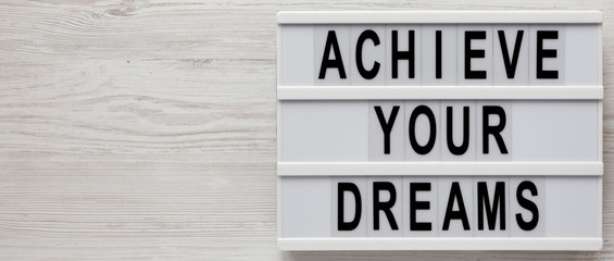 'Achieve your dreams' words on a lightbox on a white wooden background, top view. Overhead, from above, flat lay. Copy space.