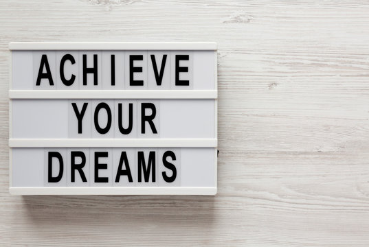 'Achieve your dreams' words on a modern board on a white wooden background, top view. Overhead, from above, flat lay. Space for text.