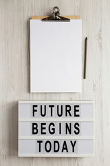 'Future begins today' words on a modern board, clipboard with blank sheet of paper on a white wooden surface, top view. Overhead, from above, flat lay.