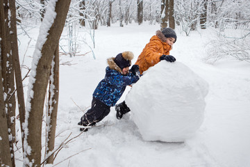 boys ride a big snowball in a winter forest