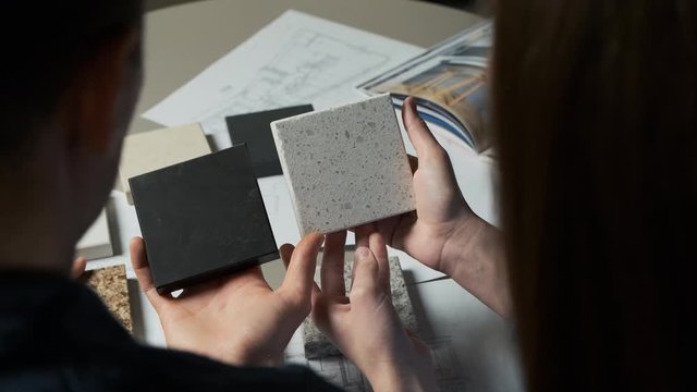 Designers compare quartz samples for kitchen countertops. A young family chooses examples from artificial stone. Close up 4k
