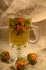 Flower tea brewed in a glass Cup and balls of flower tea on a background of rough homespun fabric. Close up.