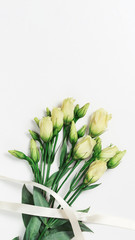 Bouquet white delicate flowers on light background with copy space. Bunch of young white eustoma roses with ribbon. Vertical format.