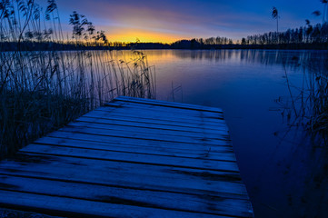 sunrise over wooden jetty and frozen lake
