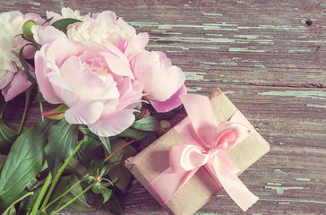 Greeting card in retro style. Handmade gift box and bouquet of pink peonies on old wooden background. Copy space flat lay