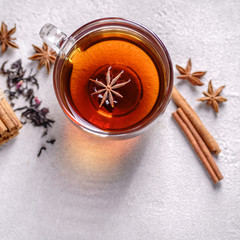 Fototapeta premium Spicy warming black tea in a glass cup with anise, cinnamon, tea stainer and sprinkled tea leaves on stone background. Cozy warming home atmosphere concept