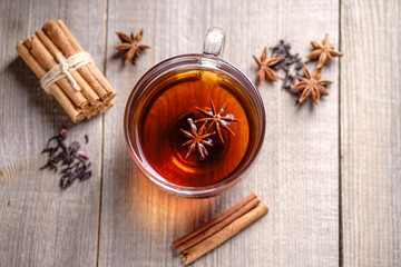 Spiced aromatic black tea. Hot warming beverage in a glass cup with anise and cinnamon on wooden background
