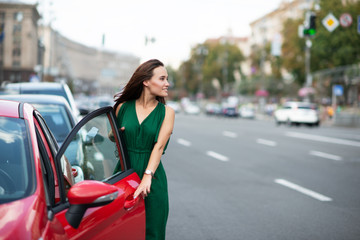 Obraz na płótnie Canvas Fashion model wearing green overall posing outdoor next to her red car on the road. Young beautiful brunette caucasian woman driver. Beautiful girl, urban portrait.