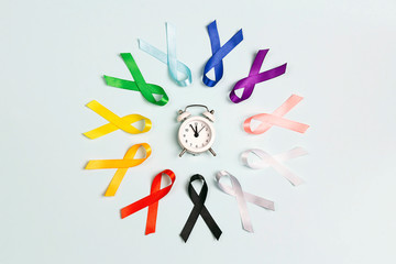 Circle of  colorful awareness ribbons with alarm clock on blue background. World cancer day concept, February 4.