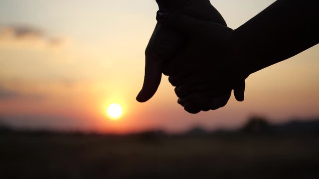 Two lovers joining Hands in 4K Slow motion. Silhouette of Man and Woman holding hands over the Sunset Background. Couple Trust, Love and Valentine's Day concept.