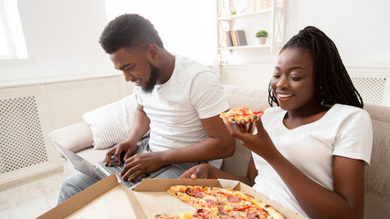 Obraz na płótnie Canvas Cheerful afro couple spending weekend with pizza and laptop
