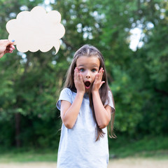 Fototapeta premium Pretty surprised thinking little girl posing summer nature outdoor with cloud of thoughts (like in comic book). Kid's portrait. Emotions, feeling and thoughts of child