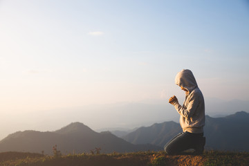 A women is praying to God on the mountain. Praying hands with faith in religion and belief in God on blessing background. Power of hope or love and devotion. - obrazy, fototapety, plakaty